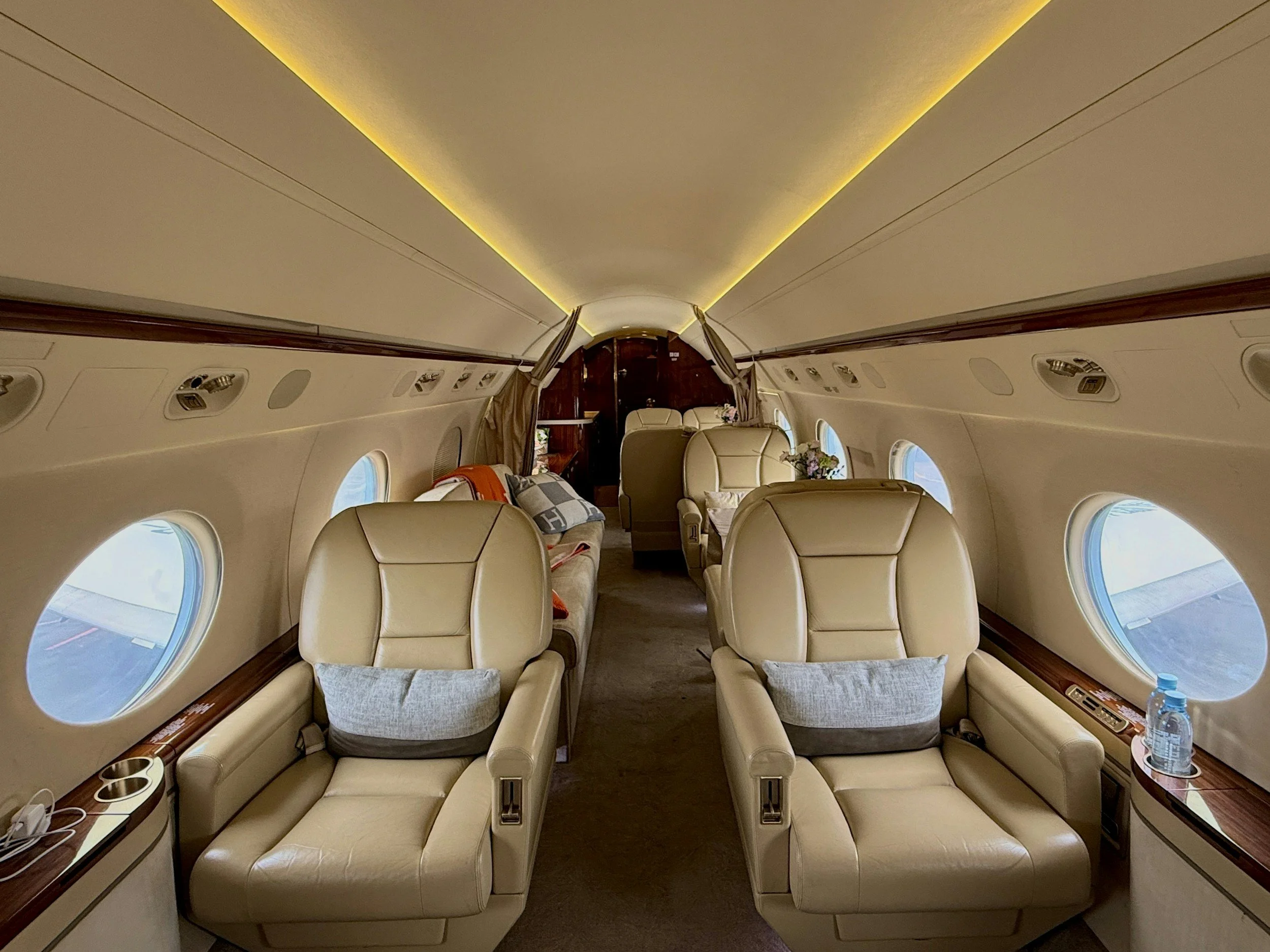 Inside the luxurious cabin of a private jet with beige leather seats, windows, and soft lighting.