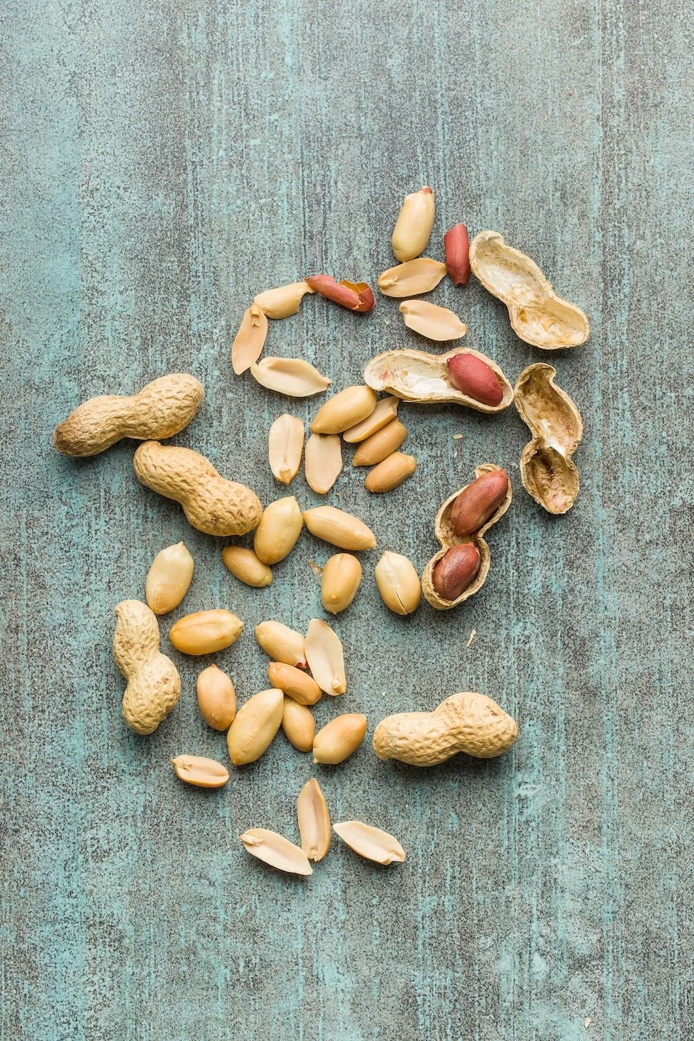 Various peanuts, some in shells and some shelled, scattered on a textured blue surface.