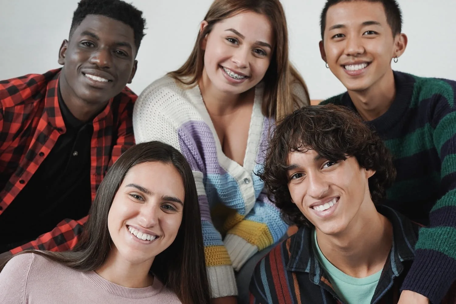 Group of six diverse young adults smiling and posing together indoors.