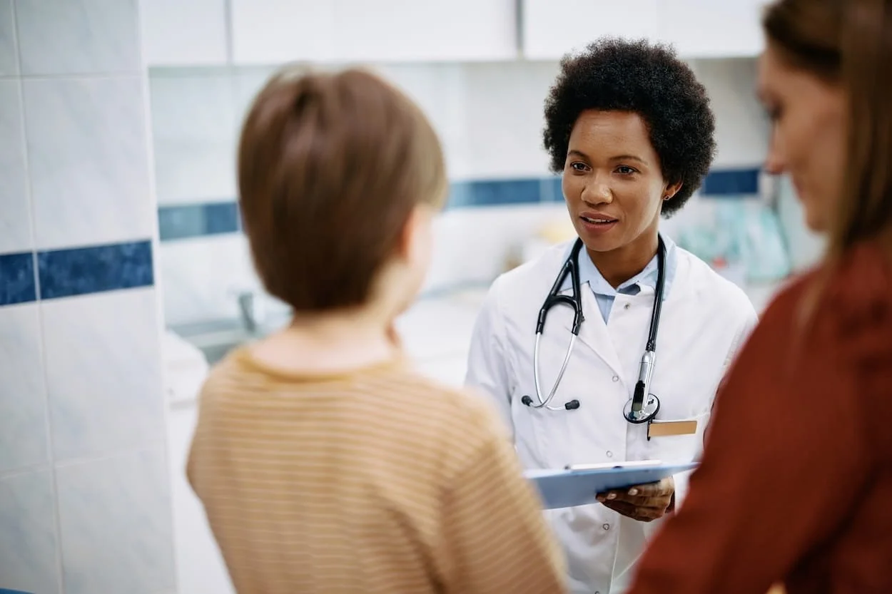 A female doctor with a stethoscope around her neck talking to two women in a medical office or clinic.