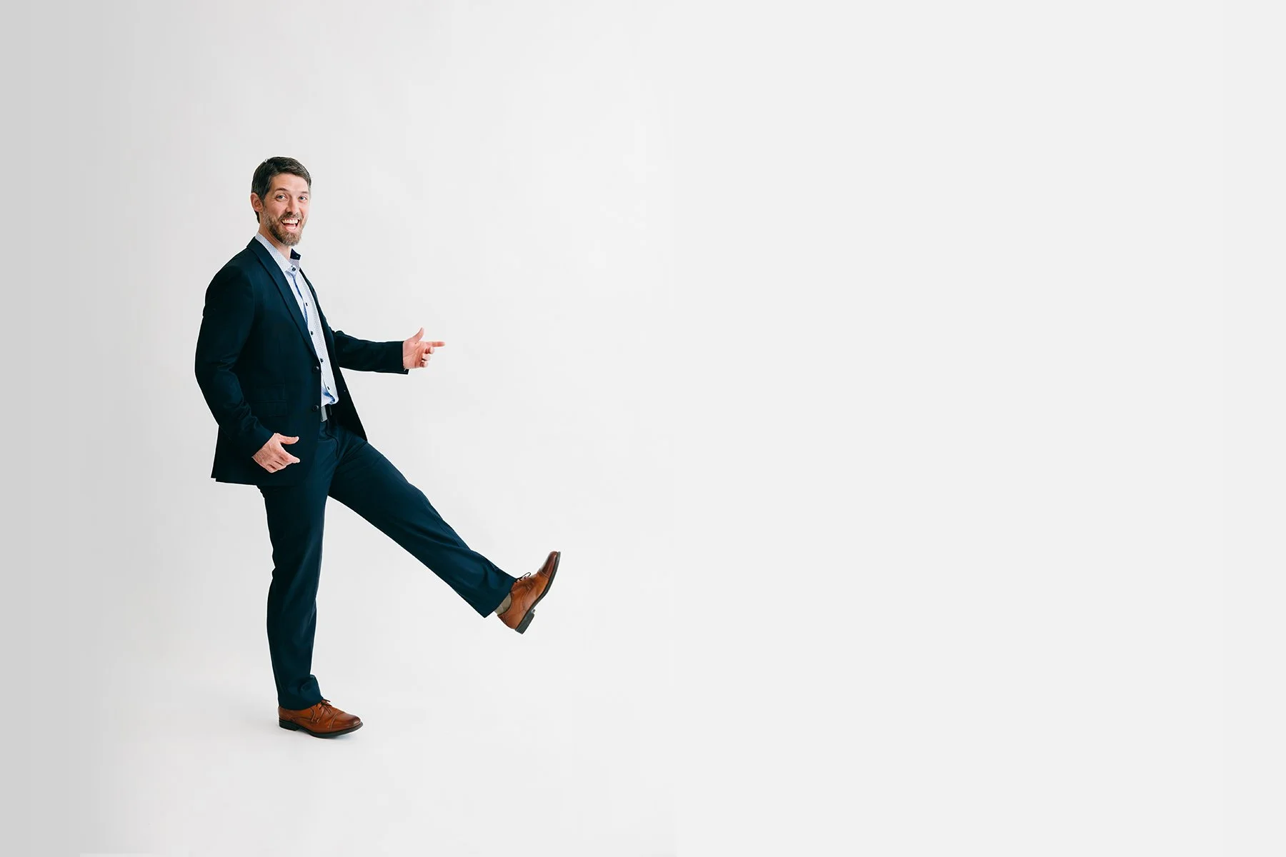 conrad bear in a dark suit smiling with his leg kicked up