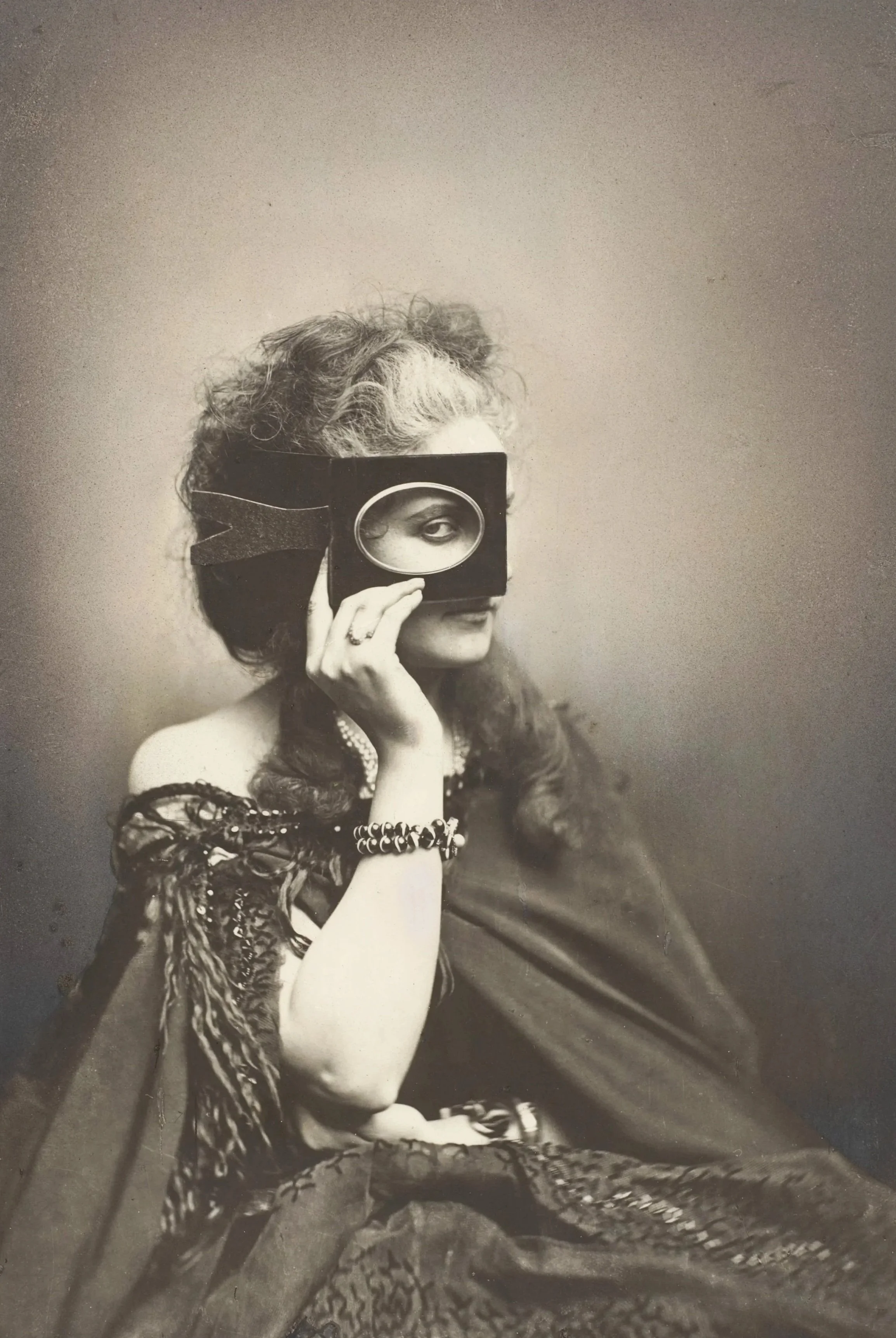 A woman in vintage clothing holding a magnifying glass over her eye, looking through it, with her other eye partially visible. She is wearing jewelry, including a bracelet and necklace, and has textured, curled hair. The photo is in black and white, with a plain background.