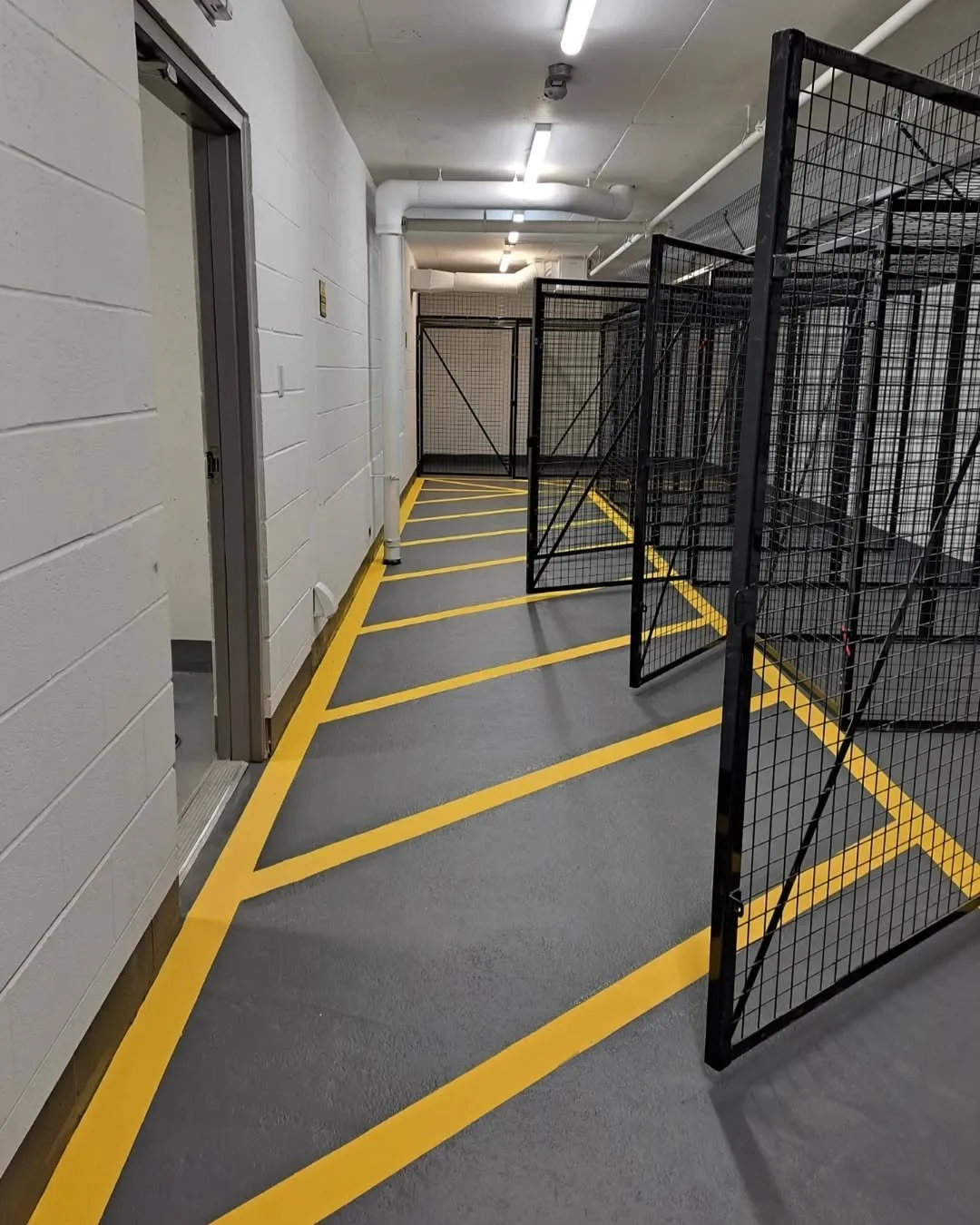An indoor area with a freshly painted gray floor marked with yellow lines and black metal fencing, possibly a storage or utility space.
