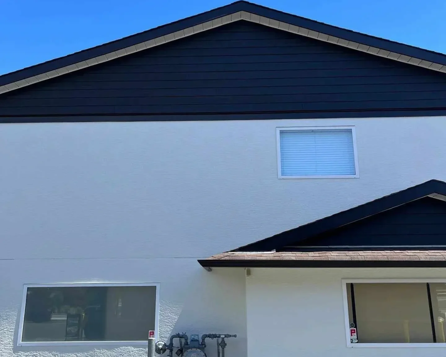 The freshly painted exterior of a two-story house with white and black siding, one large window on the lower level, a smaller window on the upper level, and a roof with dark shingles.