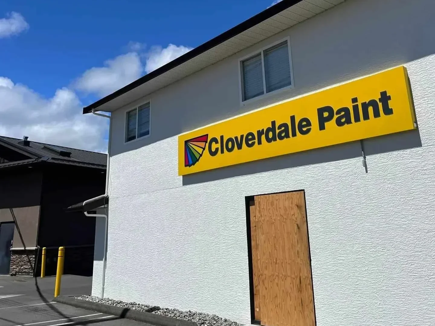 Freshly painted exterior of a commercial building with a yellow sign that reads 'Cloverdale Paint' and includes a colorful fan-shaped logo, a window, and a wooden boarded-up door.
