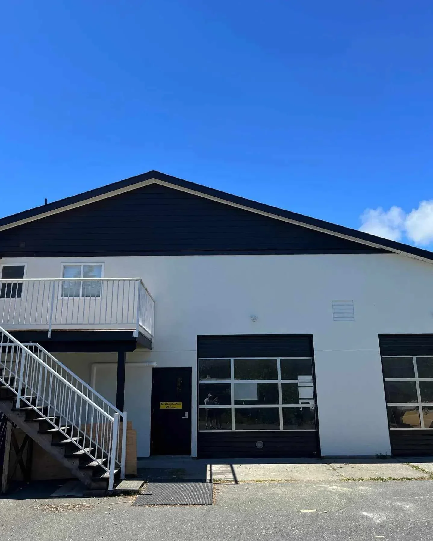 Modern two-story building with black and white exterior, glass garage door, and external staircase under a clear blue sky.
