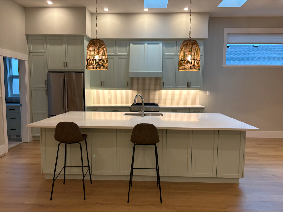 Modern kitchen with light-colored cabinets, a large island with white countertop, two woven pendant lights, and stainless steel refrigerator.