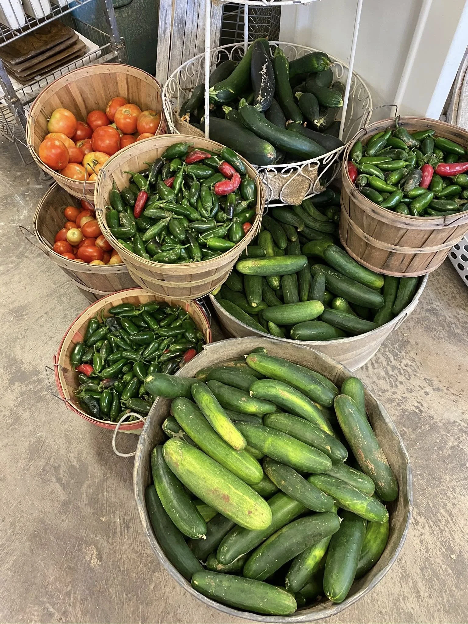 Multiple baskets and bins filled with fresh vegetables including cucumbers, jalapeños, tomatoes, and zucchini.