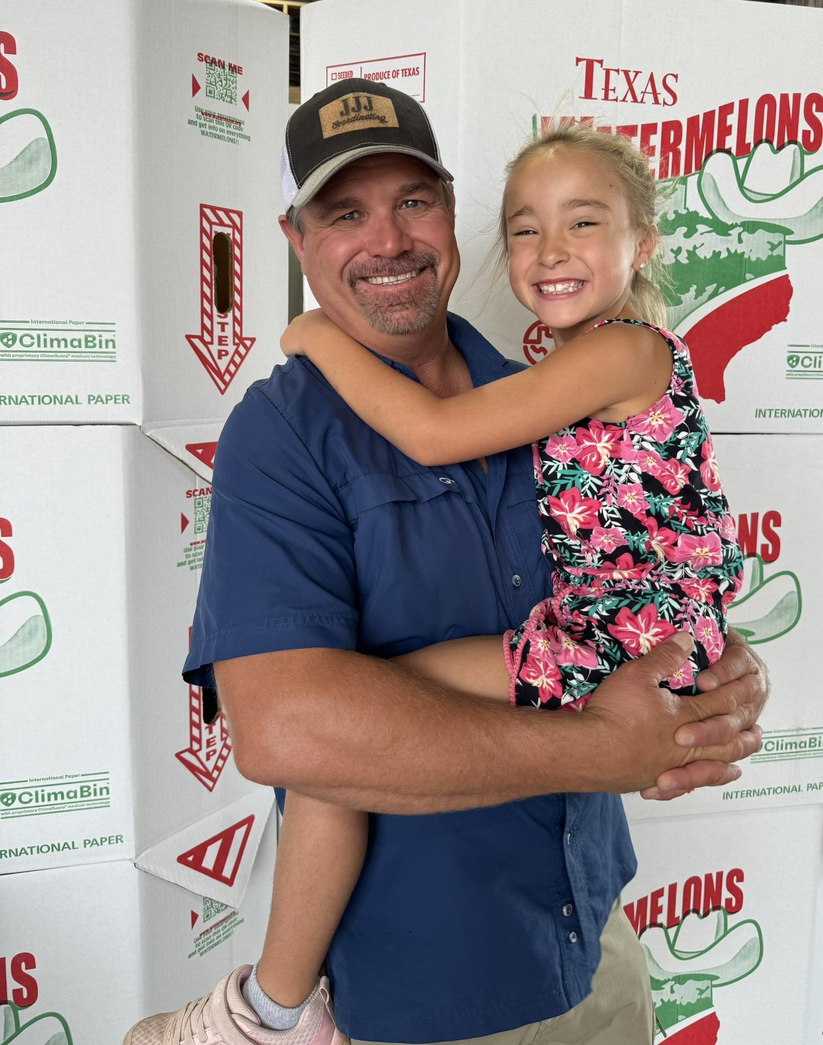 A man holding a smiling young girl in front of boxes labeled 'Texas Watermelons' and 'ClimaBin.'