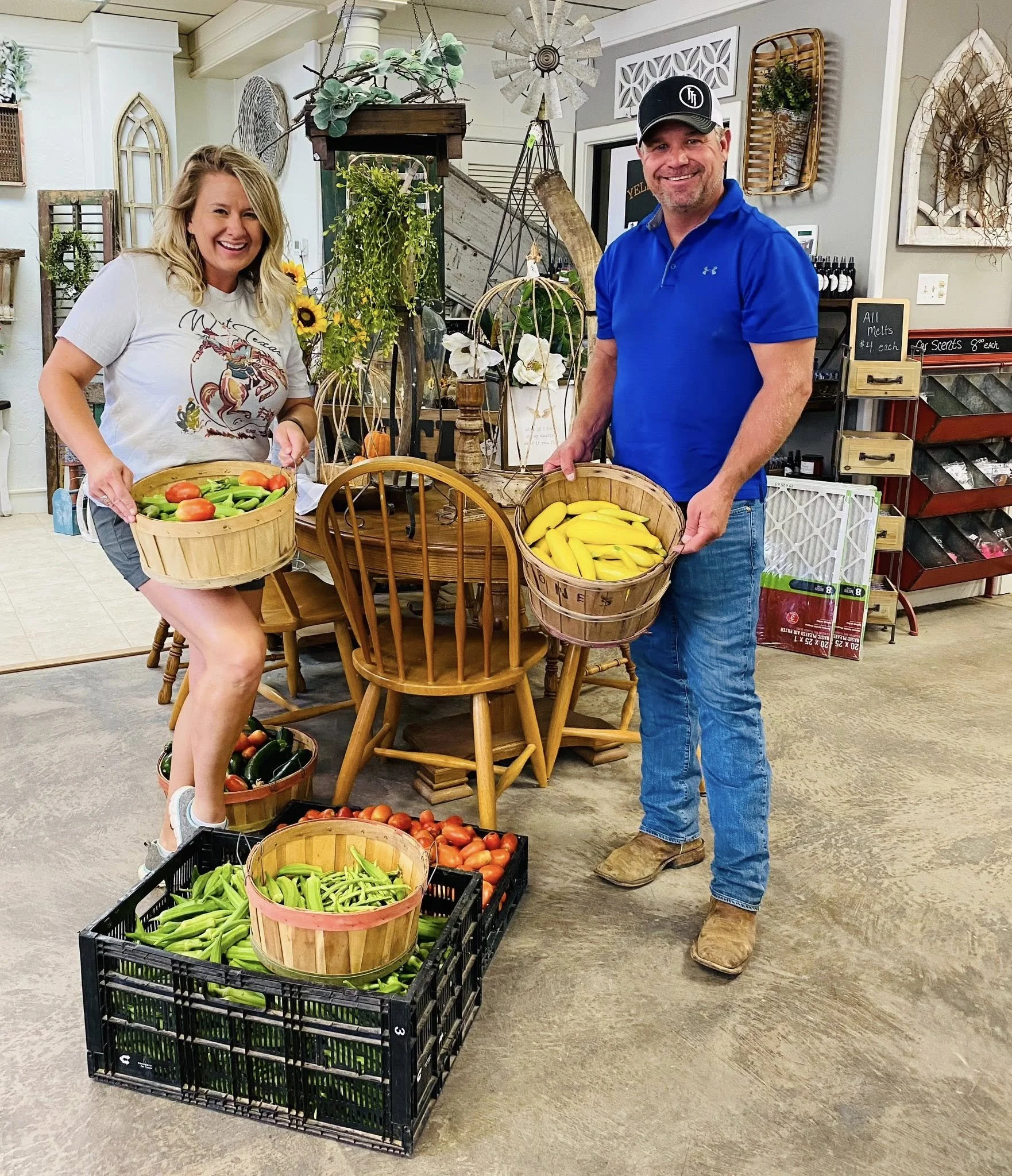 A man and woman holding baskets of yellow bananas and tomatoes in a store with various decorations and produce around them.