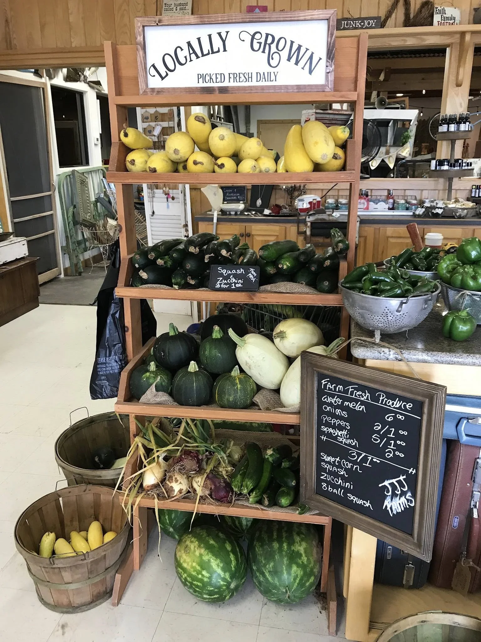 Display of fresh farm produce including yellow melons, zucchinis, green peppers, white squash, purple and green turnips, and watermelons at a local market with a sign.