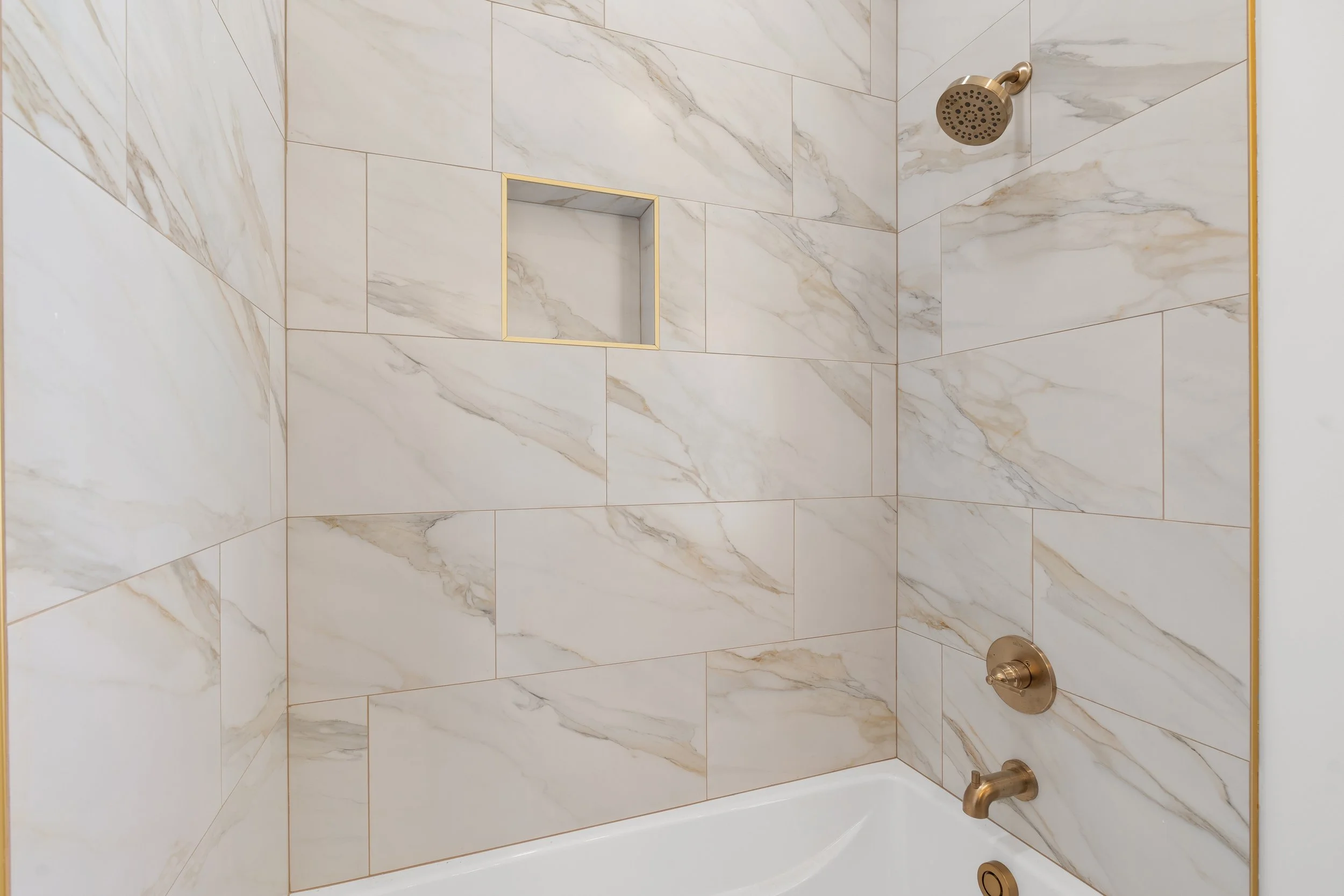 Bathroom shower with marble tiles, built-in niche, and bronze fixtures.