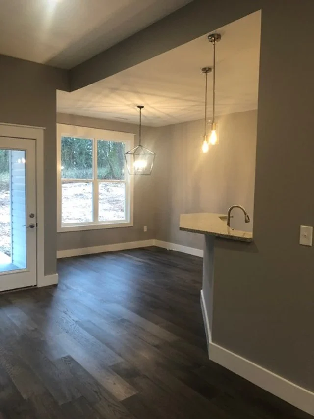 Empty living room with large window, hardwood floors, and modern lighting fixtures.