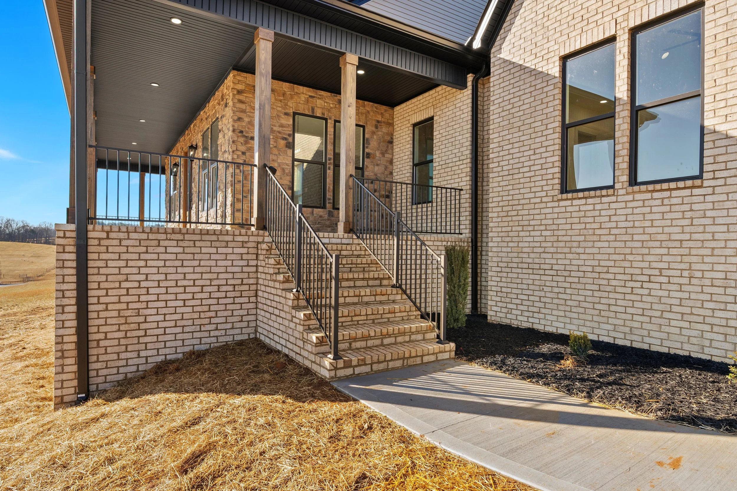 Exterior view of a modern house with brick walls, stairs, and a porch with black metal railing.