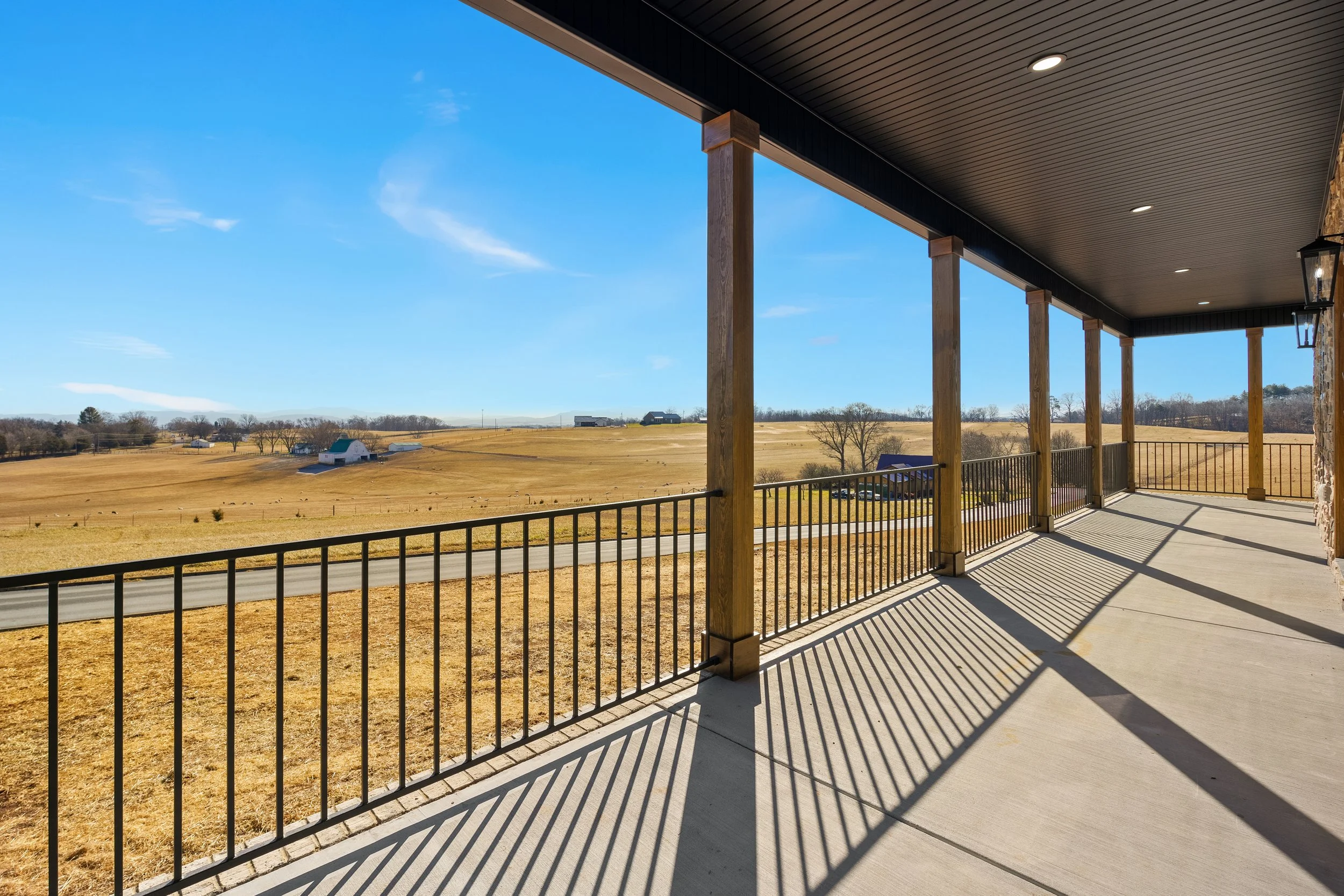 Empty balcony with metal railing overlooking a rural field and blue sky.