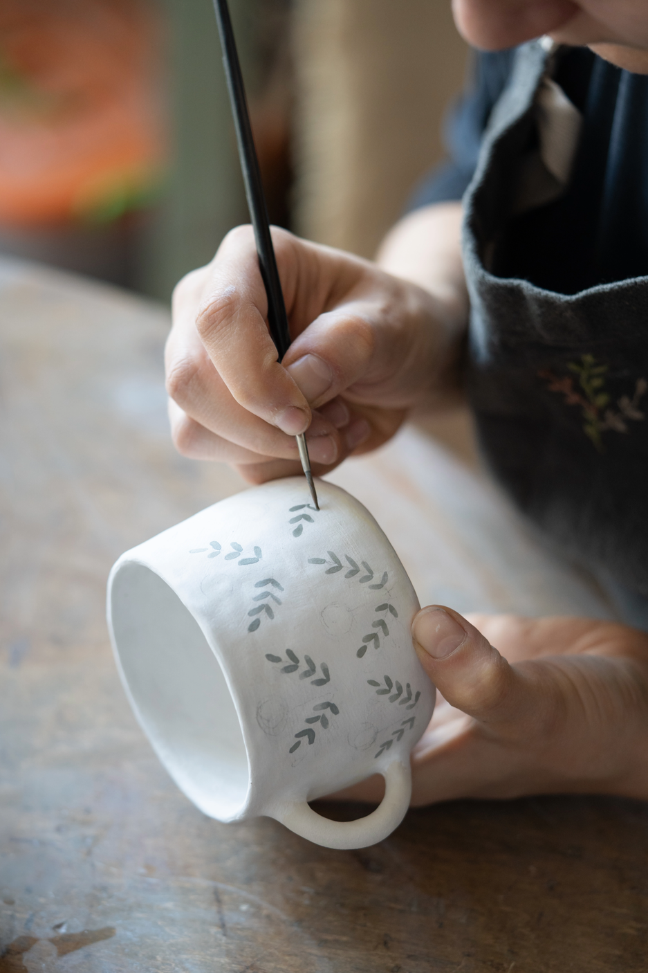 Person painting a decorative pattern with leaves on a ceramic mug.