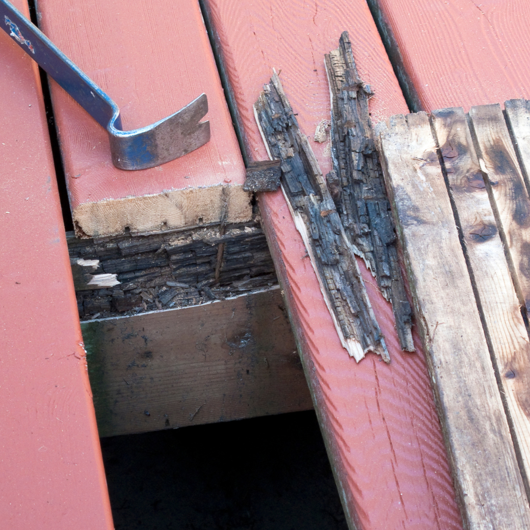 Close-up of damaged wooden deck boards, with a pry bar tool on the left side.