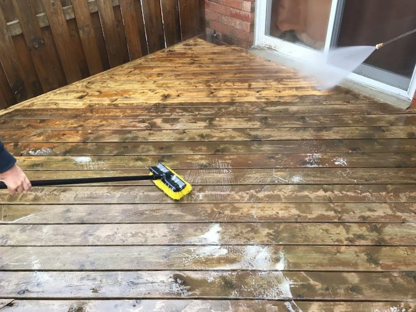 Person using a pressure washer to clean or wash a wooden deck outdoors.