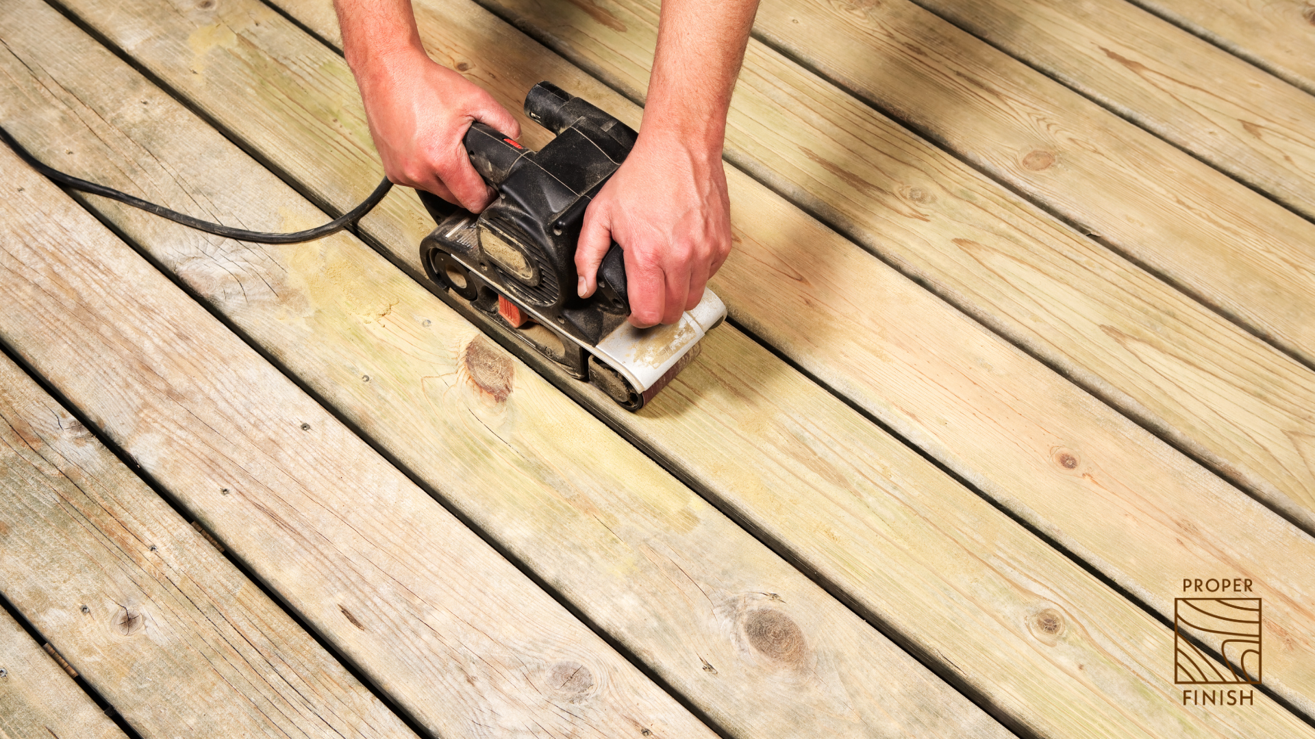 A person using a sander to smooth a wooden deck made of multiple planks.