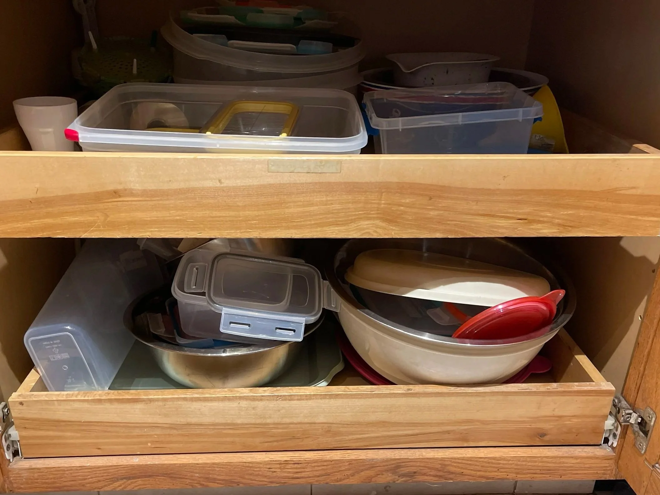 Photo of a disorganized overflowing kitchen cabinet space with mixed up containers and lids.