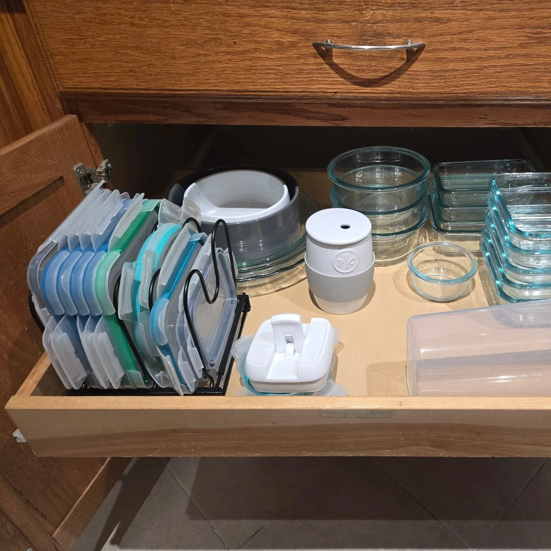 Photo of a kitchen cabinet shelf with well organized easy to find glass food containers with their lids on a rack.