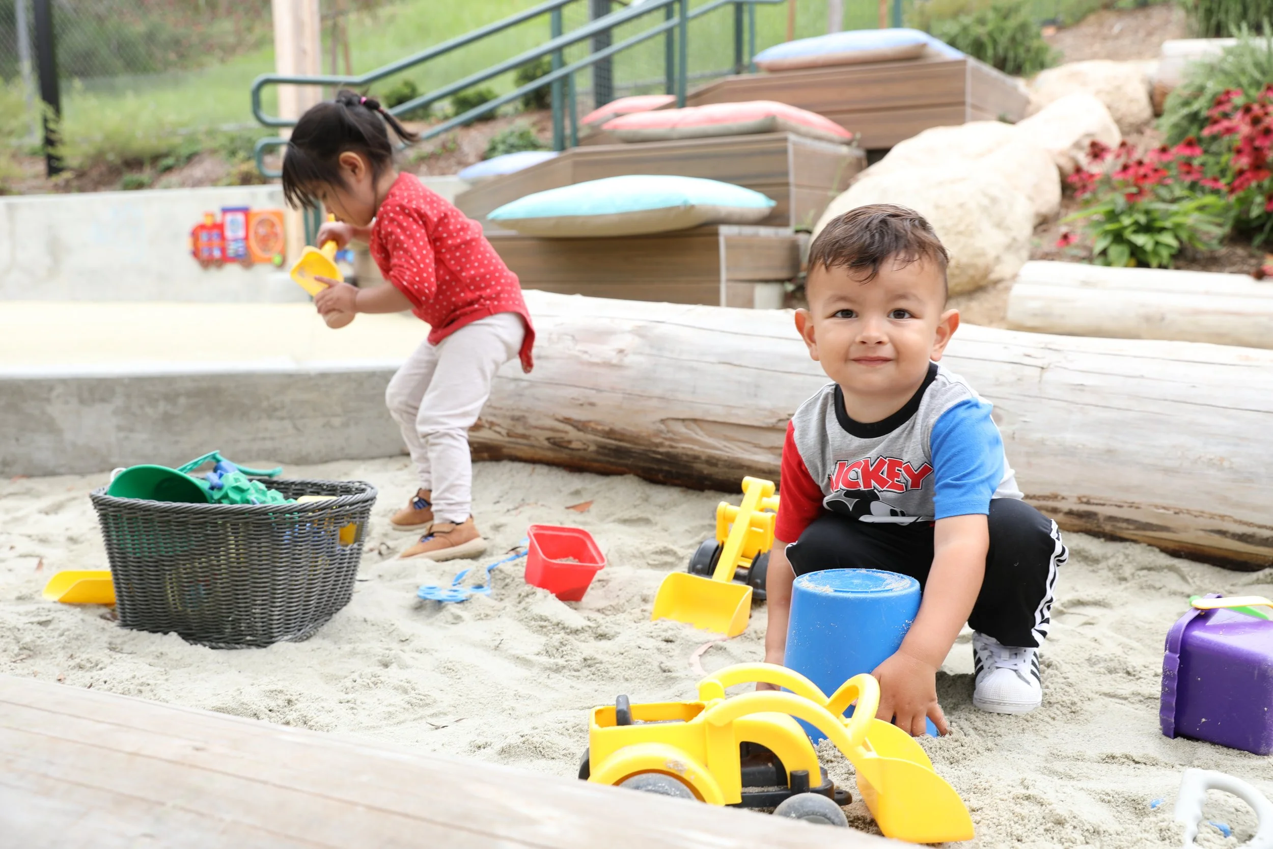 Children engaging in sensory sand play with buckets, shovels, and toy trucks