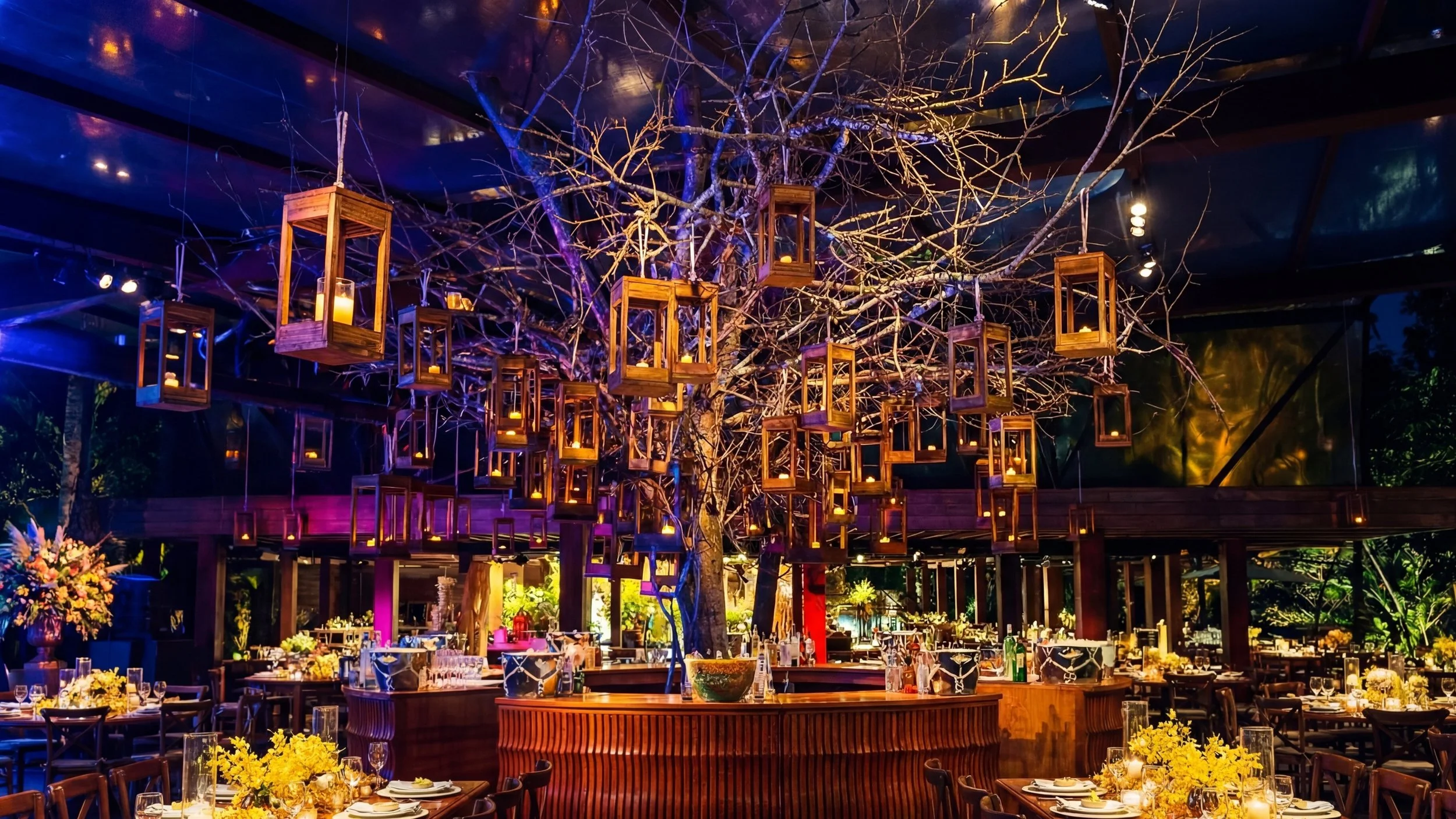 Jardim de árvores secas decorado com lanternas de madeira suspensas com velas acesas, em um espaço de jantar elegante ao ar livre com mesas preparadas para os convidados.