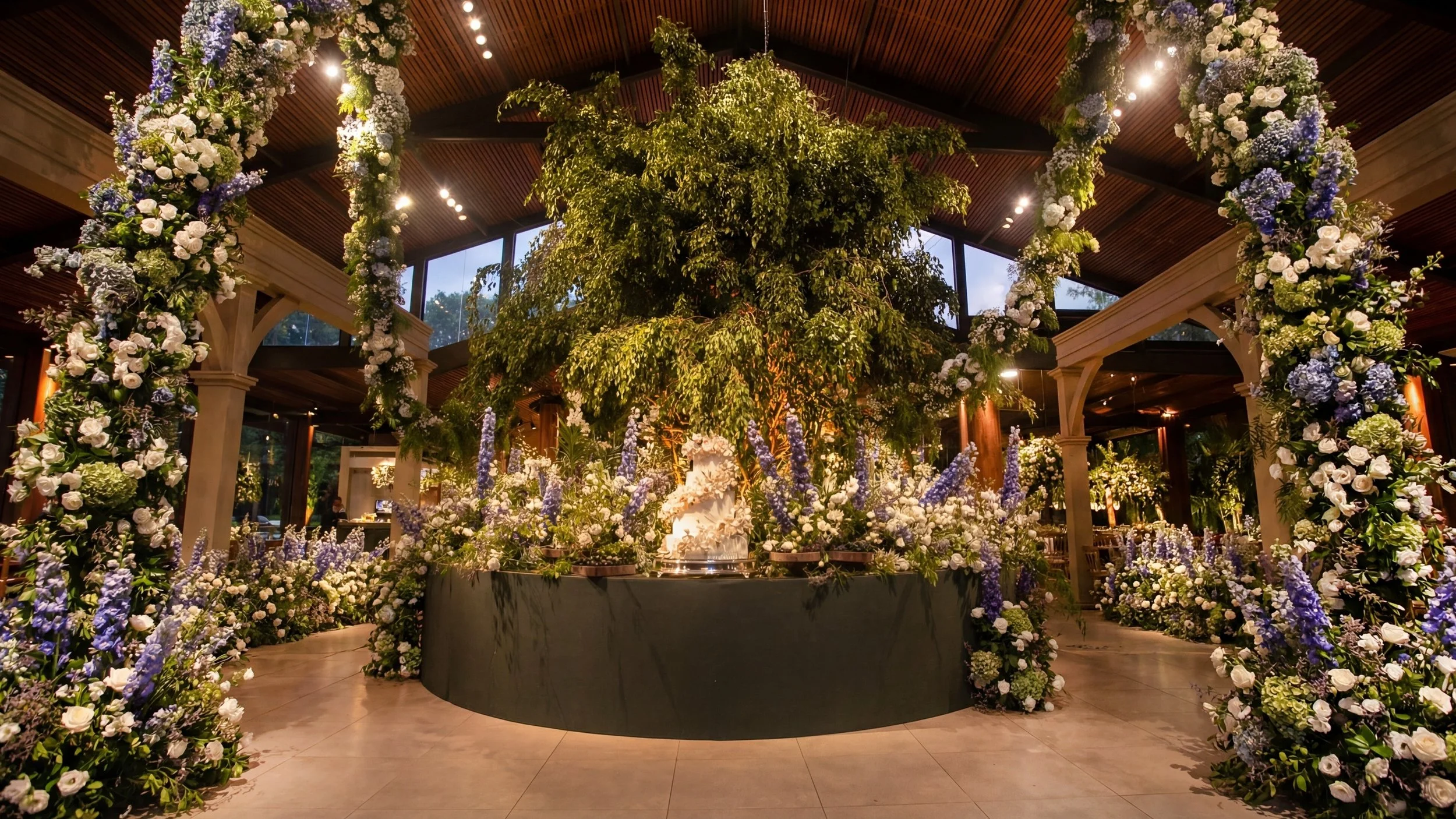 Decoração de casamento com arco floral, muitas flores brancas e roxas, centro de mesa com árvore decorativa, ambiente interno elegante com iluminação quente e janelas grandes