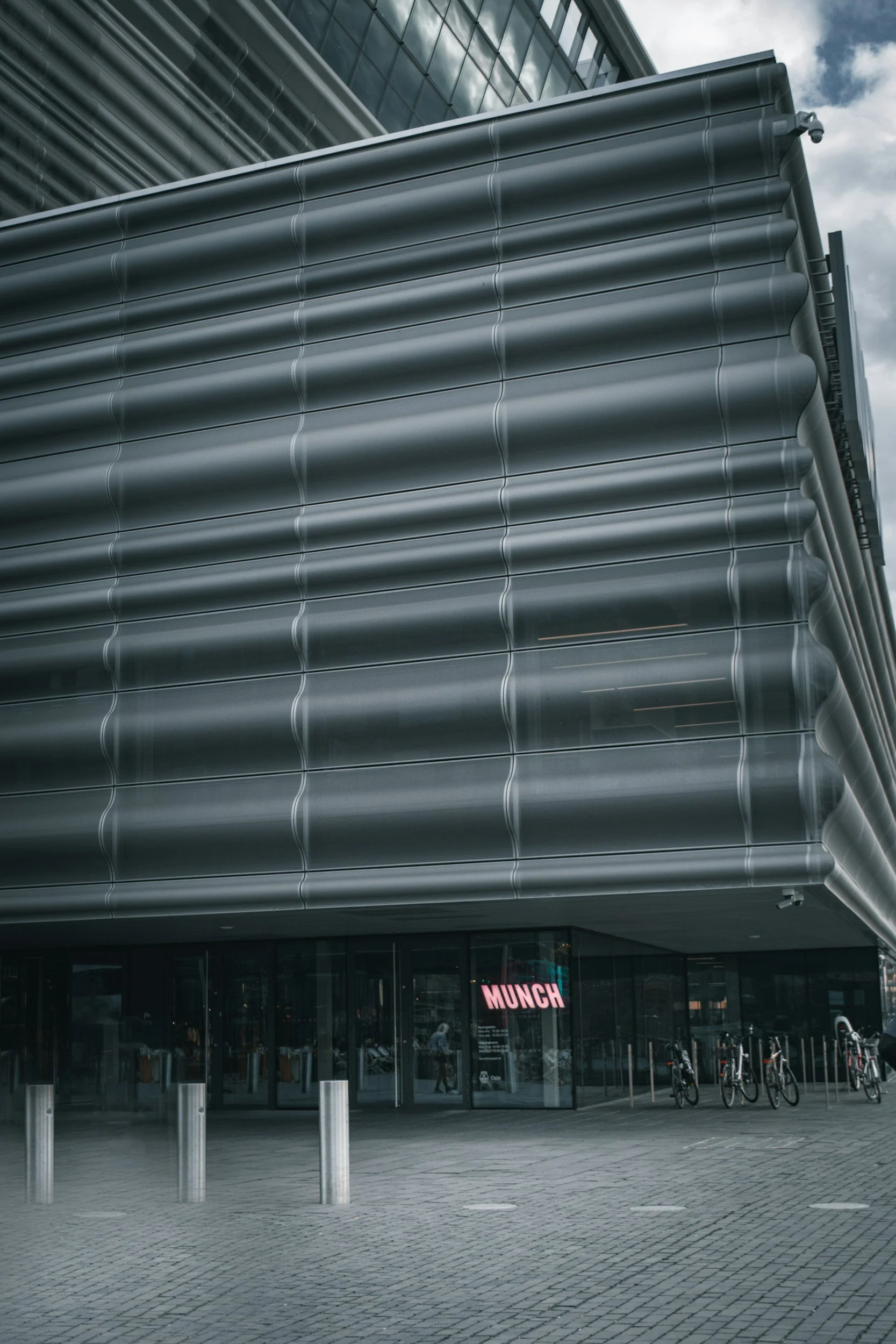 Biletet viser Munchmuseet i Oslo frå bakkenivå, med neonskilt og den grå, rare metallfasaden.