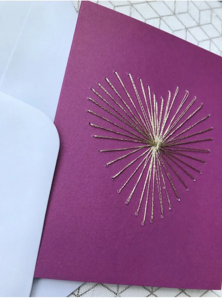 pink card with gold starburst stitching nested inside white envelope