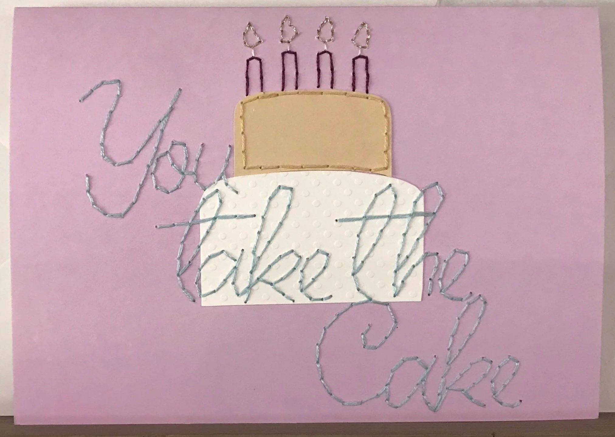 Embroidered words "you take the cake" on top of image of cake with 4 lit candles