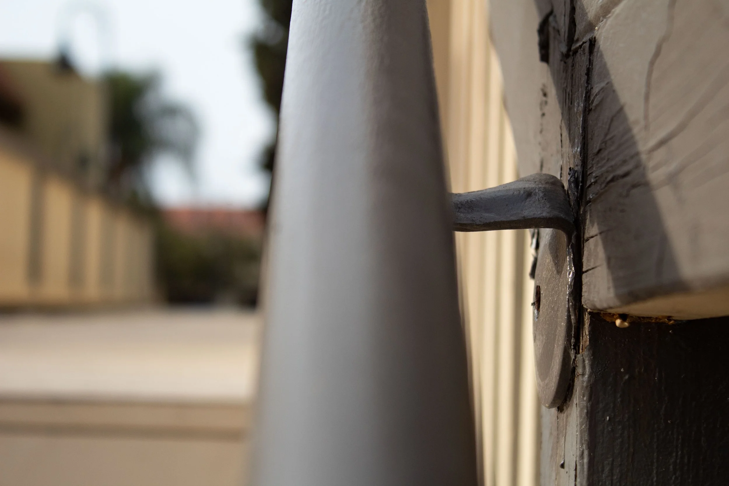 Close-up of a metal latch on a wooden door or gate, with blurred background of trees and buildings.