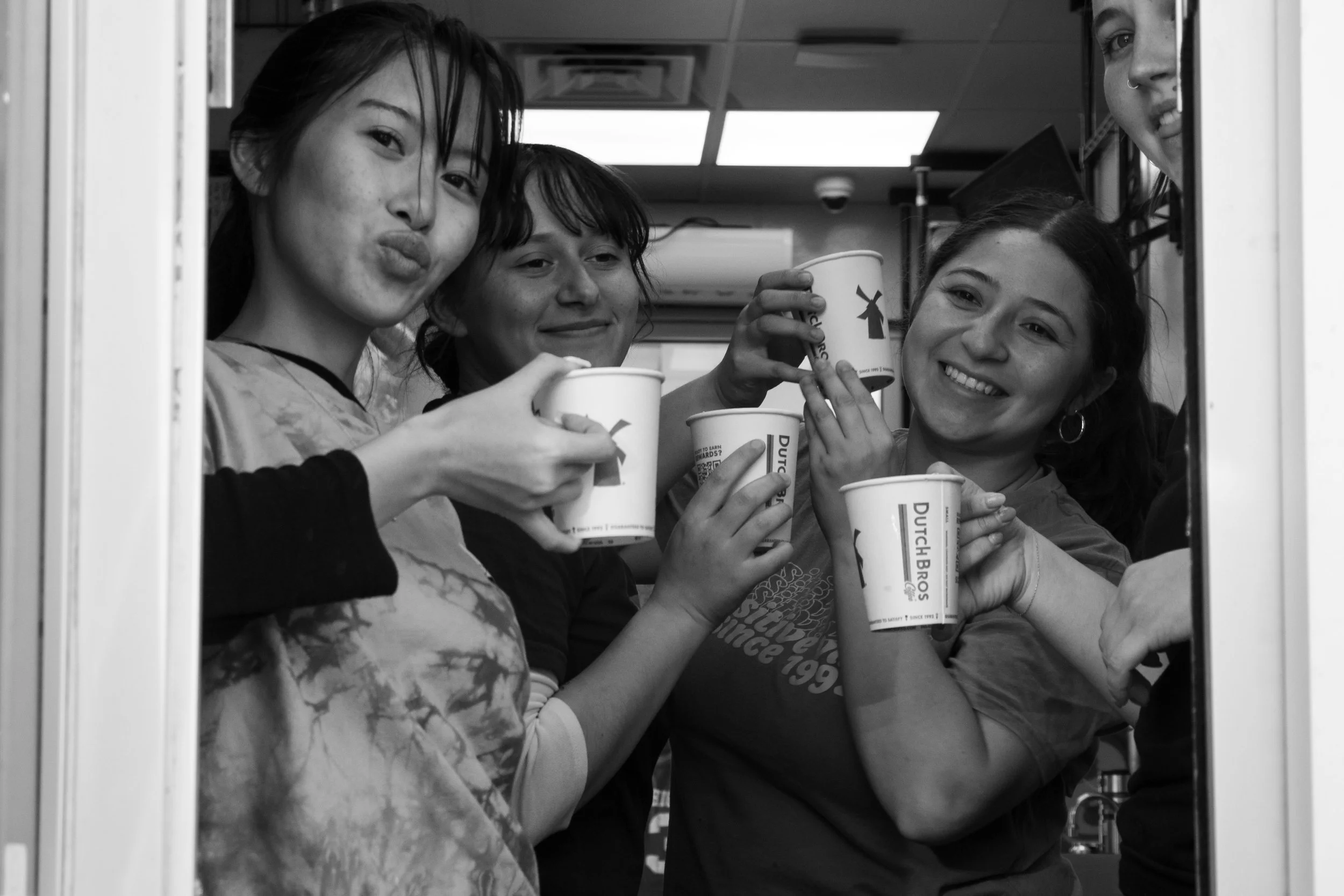 Group of four women smiling and holding cups of coffee inside a fast food restaurant, with a woman on the left blowing a kiss.