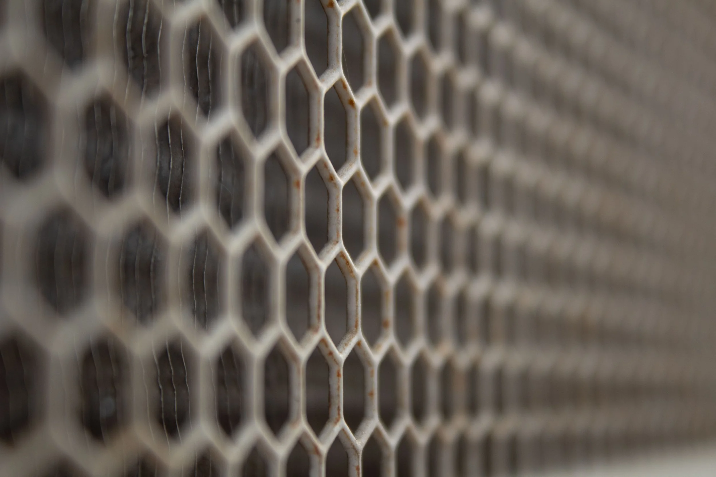Close-up of a rusty metal honeycomb pattern on a fence or grate.