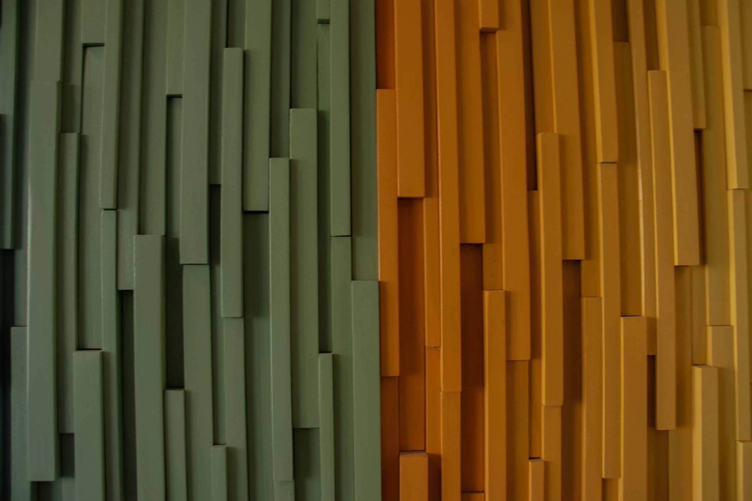 A decorative wall with vertical rectangular wooden panels, painted in green on the left side and yellow on the right side.