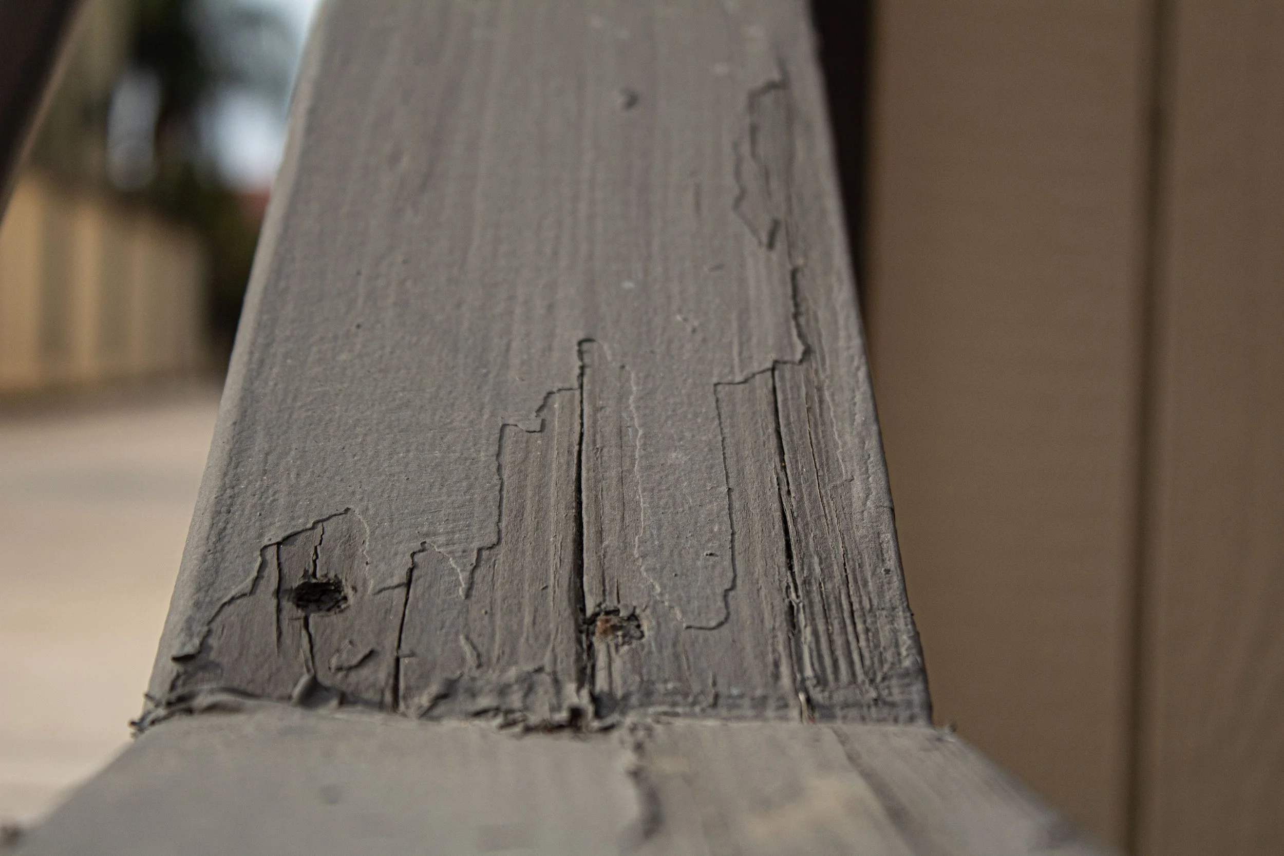 Close-up of a weathered wooden railing with peeling paint and cracks.