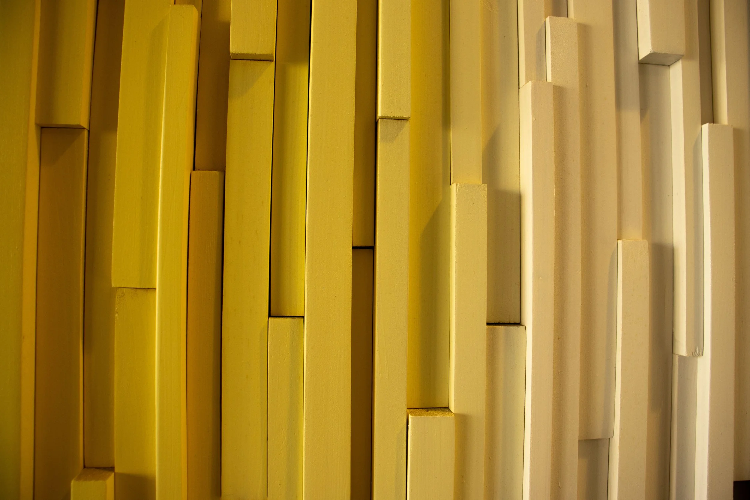 Close-up of a decorative wall with vertically arranged rectangular wooden slats painted in shades of yellow and beige.