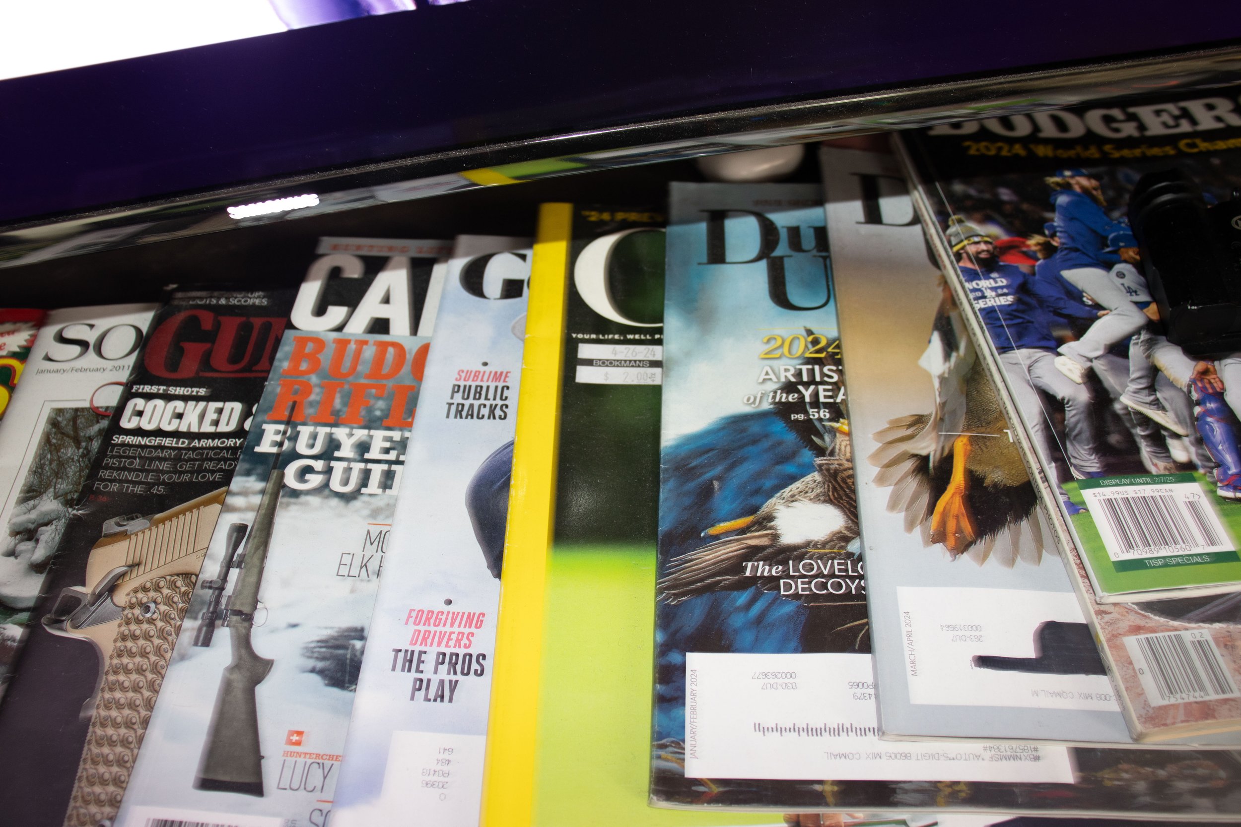 Stack of magazines on a table, including Guns & Ammo, Game Informer, and Sports Illustrated, with colorful covers.