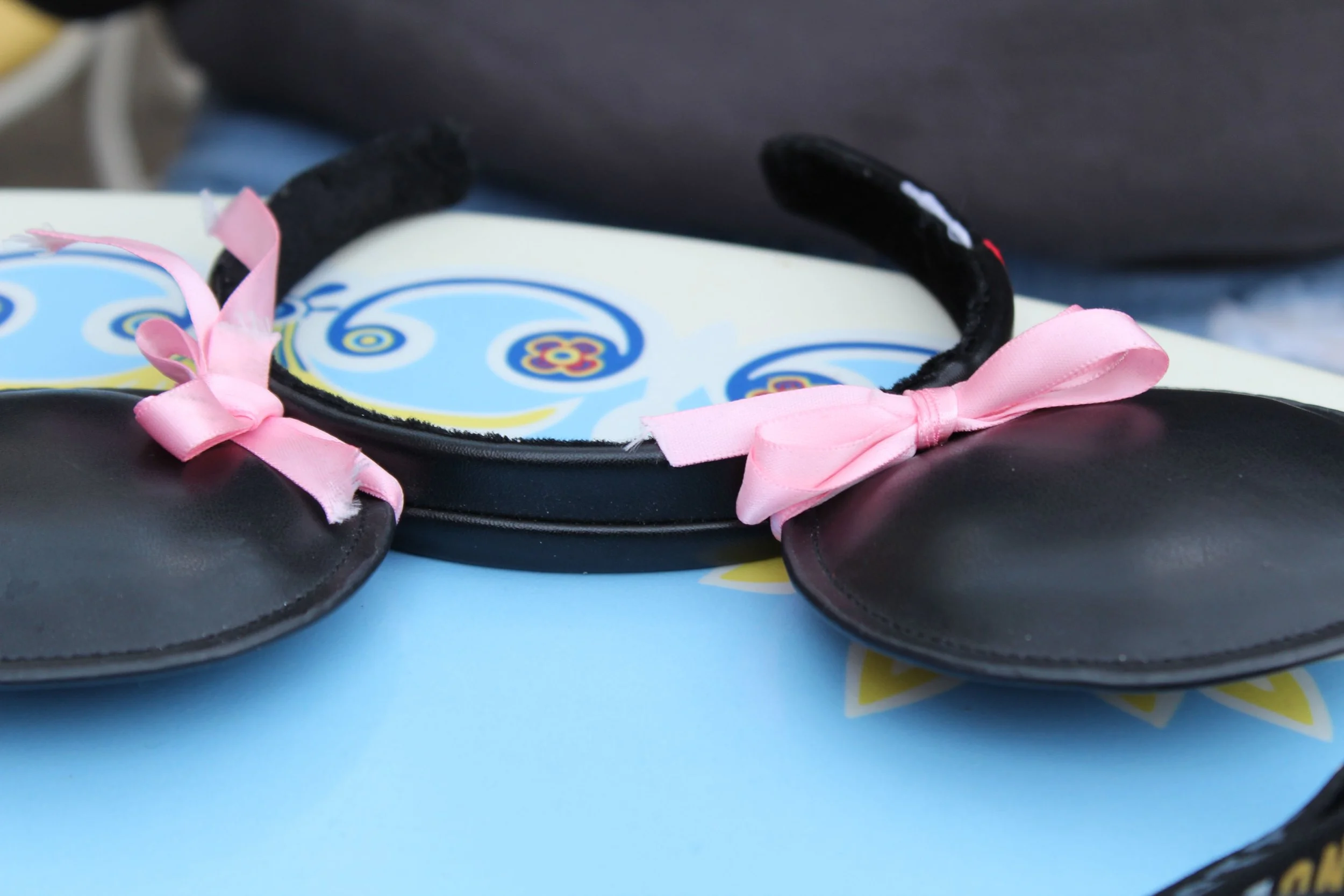 Black headband with pink bows and black ears, resembling Minnie Mouse, resting on a colorful paper with a swirl design.