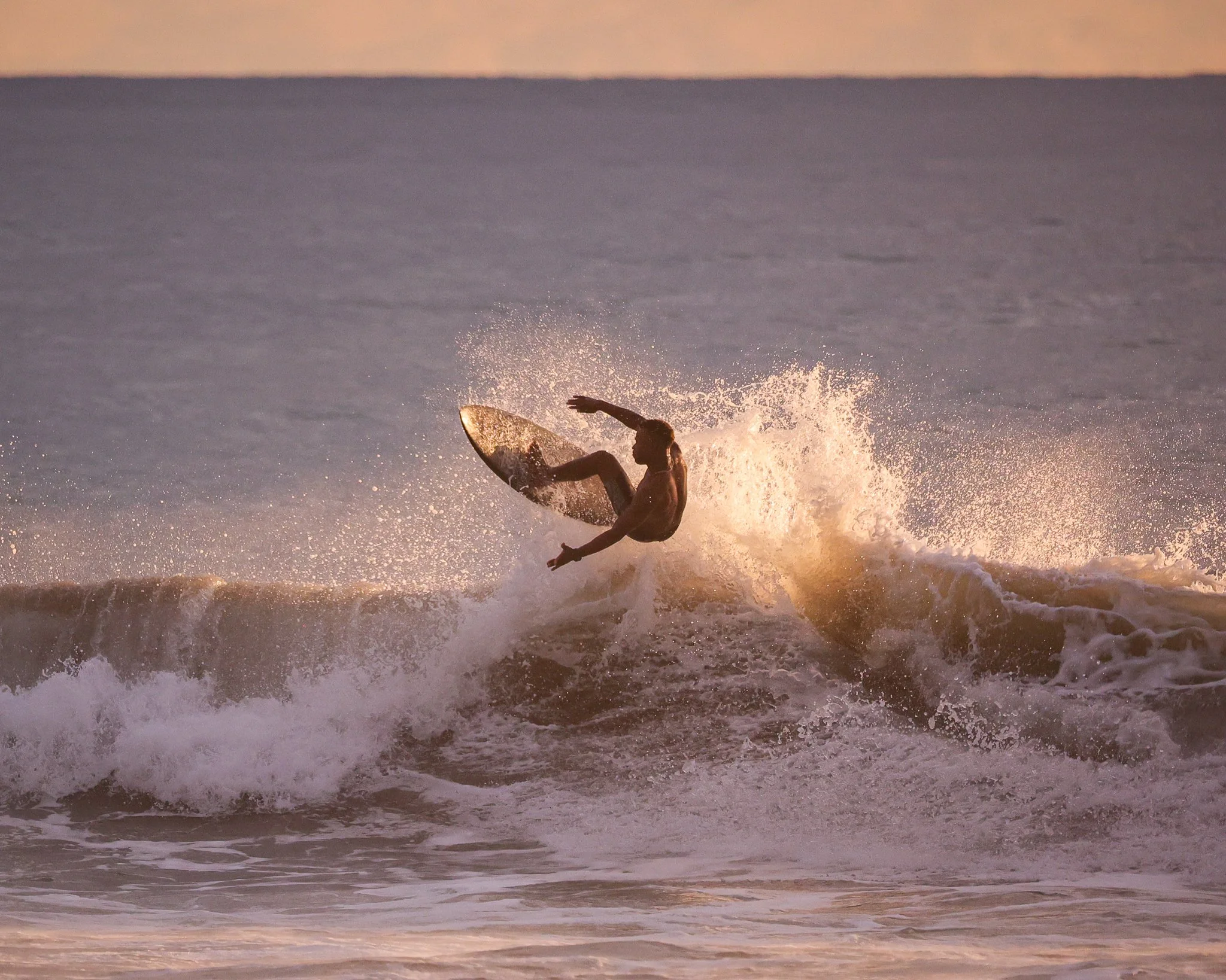 A person surfing on a wave at sunrise or sunset with water splashing around them.