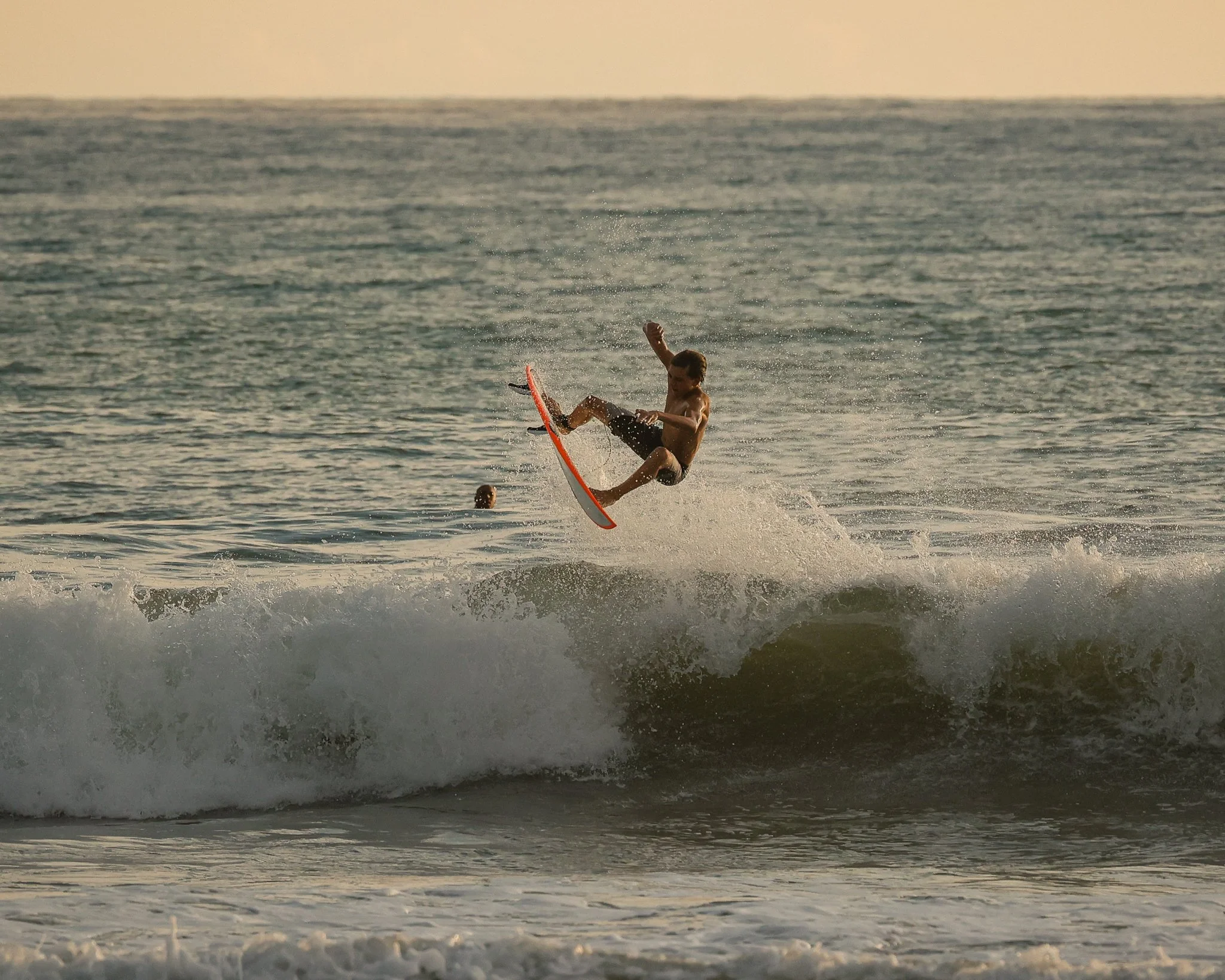Young man surfing on a wave in the ocean during sunset