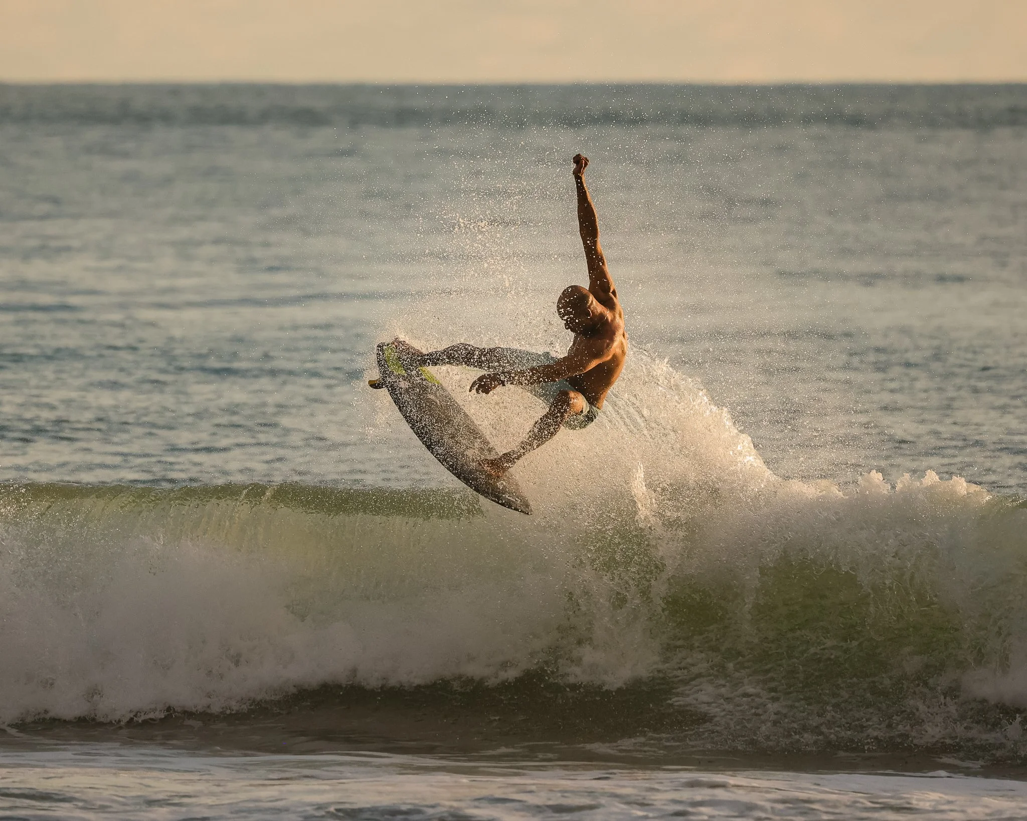 A man surfing on a wave in the ocean at sunset.