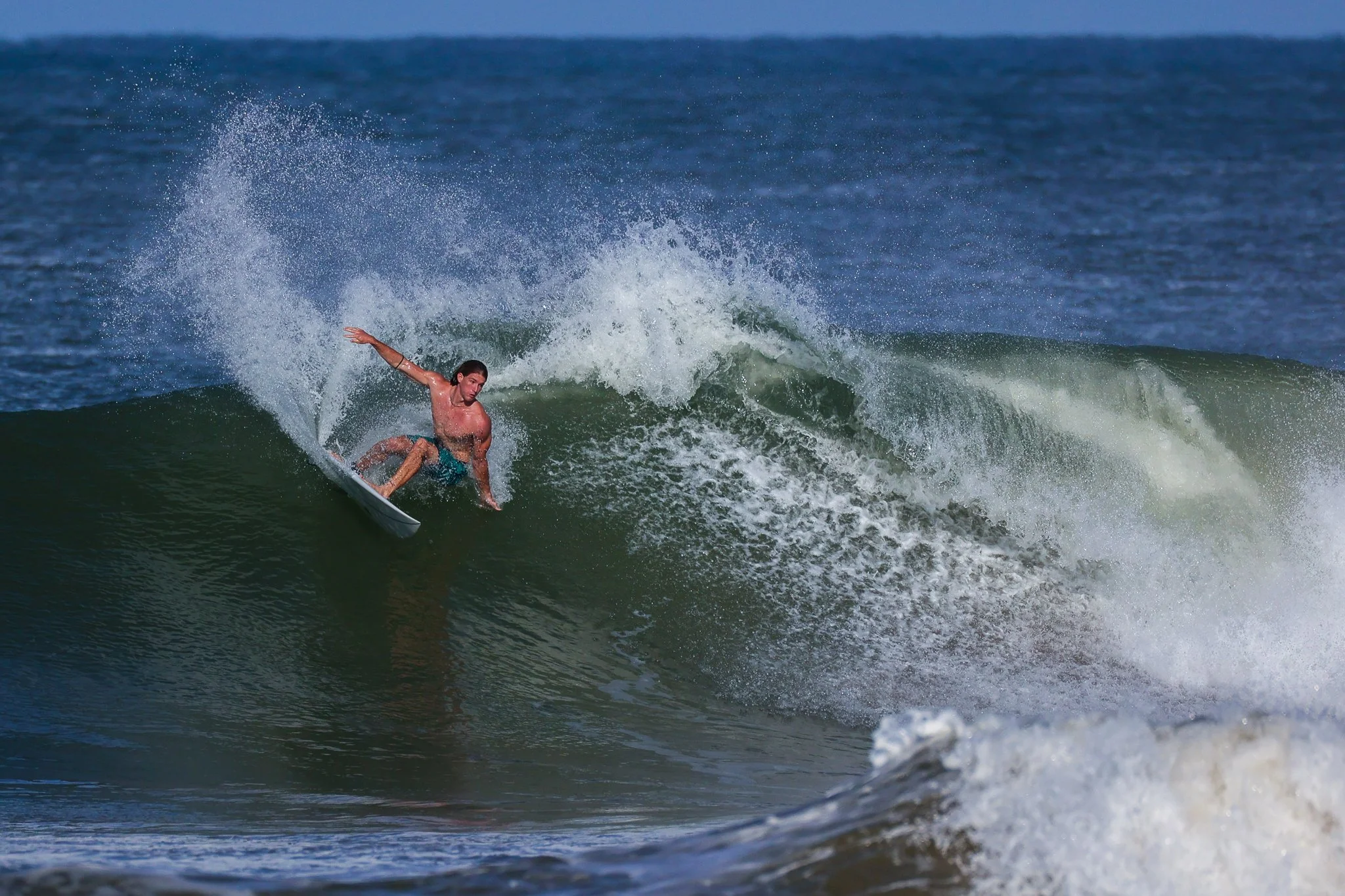 A male surfer wearing blue shorts riding a wave on a surfboard in the ocean.
