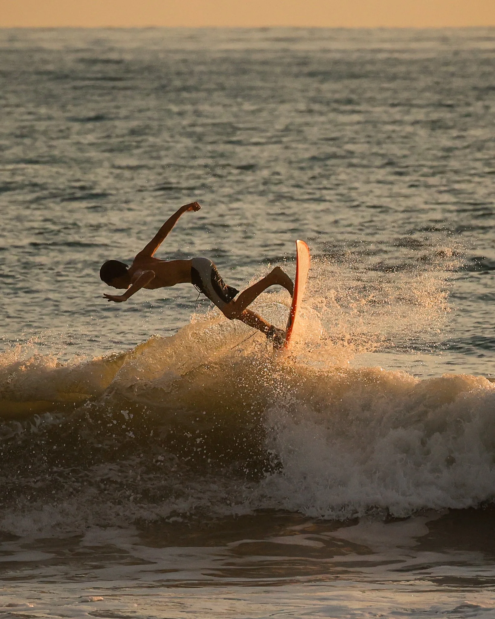 A person surfing on a wave at the beach during sunset, balancing on a red surfboard.