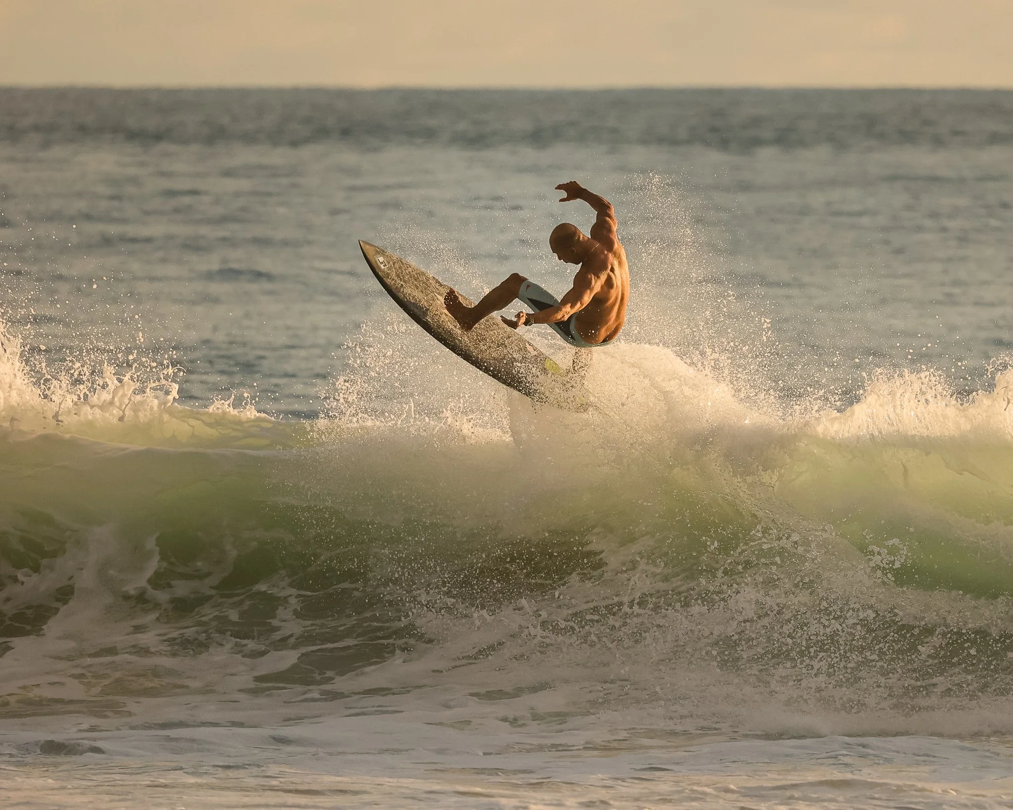 A male surfer riding a wave at sunset on the ocean.