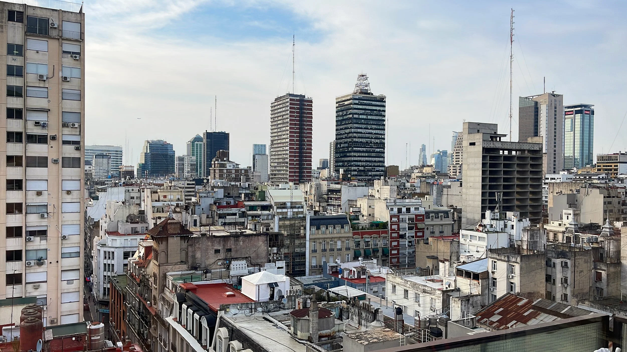 City skyline with tall modern buildings and older low-rise structures, under a partly cloudy sky.