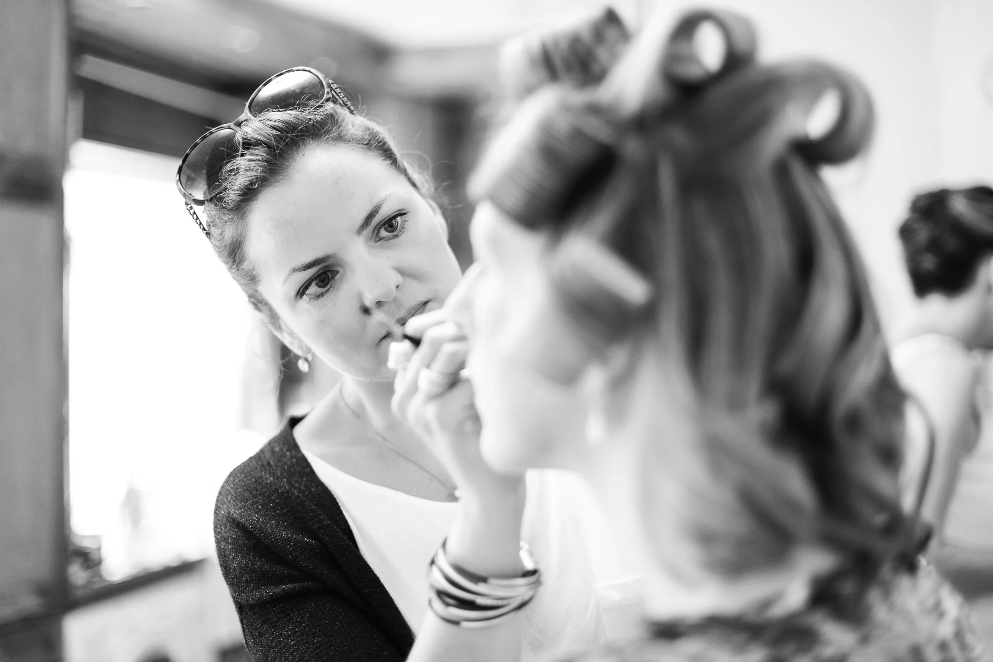 A woman is applying makeup on another woman's face in a salon or makeup studio.