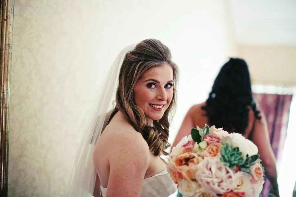 A smiling bride holding a bouquet of pink, white, and green flowers.