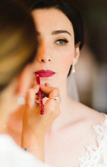 Bride having makeup applied with pink lipstick by makeup artist