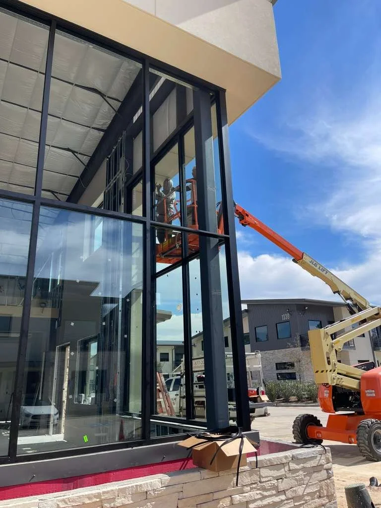 Glassworks workers using a cherry picker to install or repair large glass windows on a building.